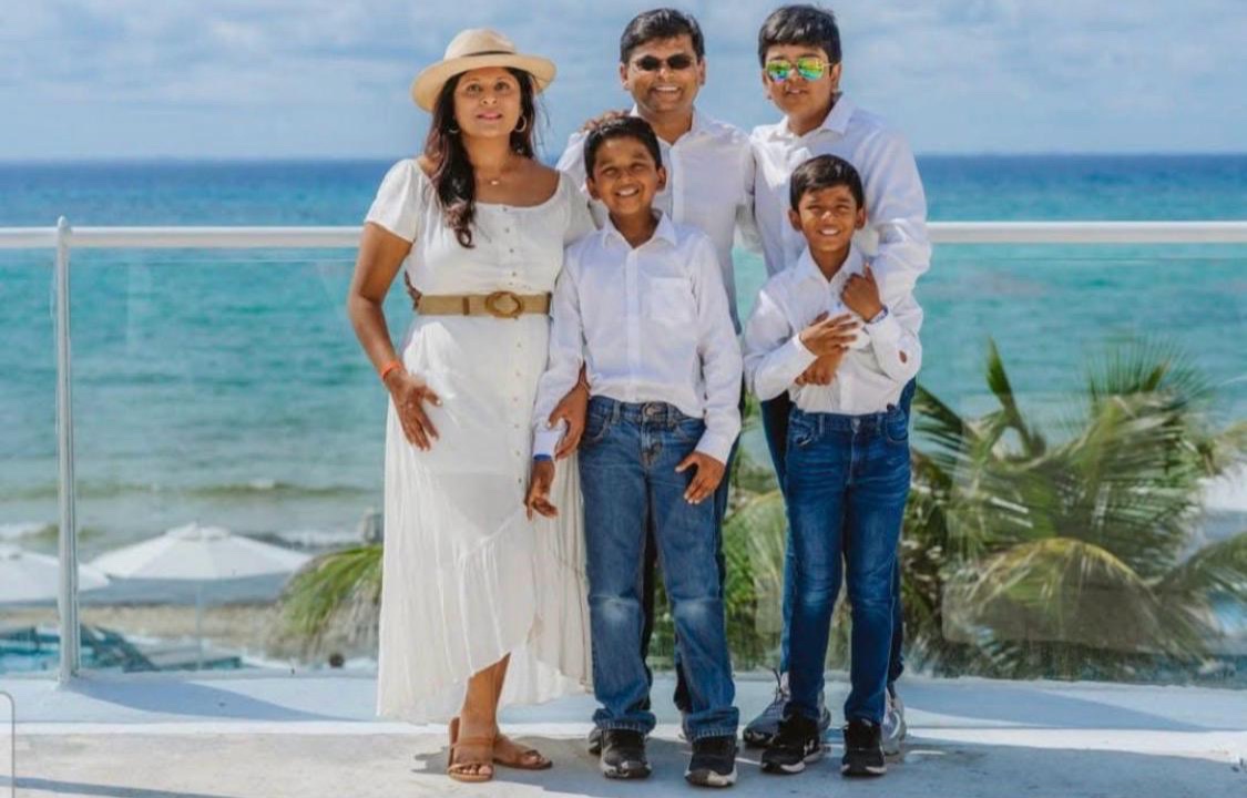 Amee with her husband and three sons, all dressed in white, on a terrace above a turquoise sea.